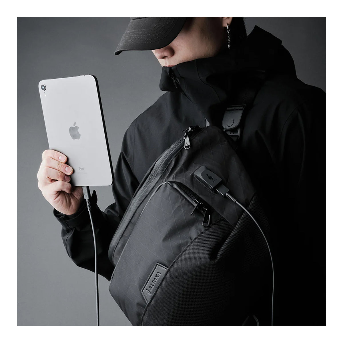 Alpaka Bravo Sling Max V2, слінг на плечі, чоловік тримає планшет, кабель заряджання виведений через порт